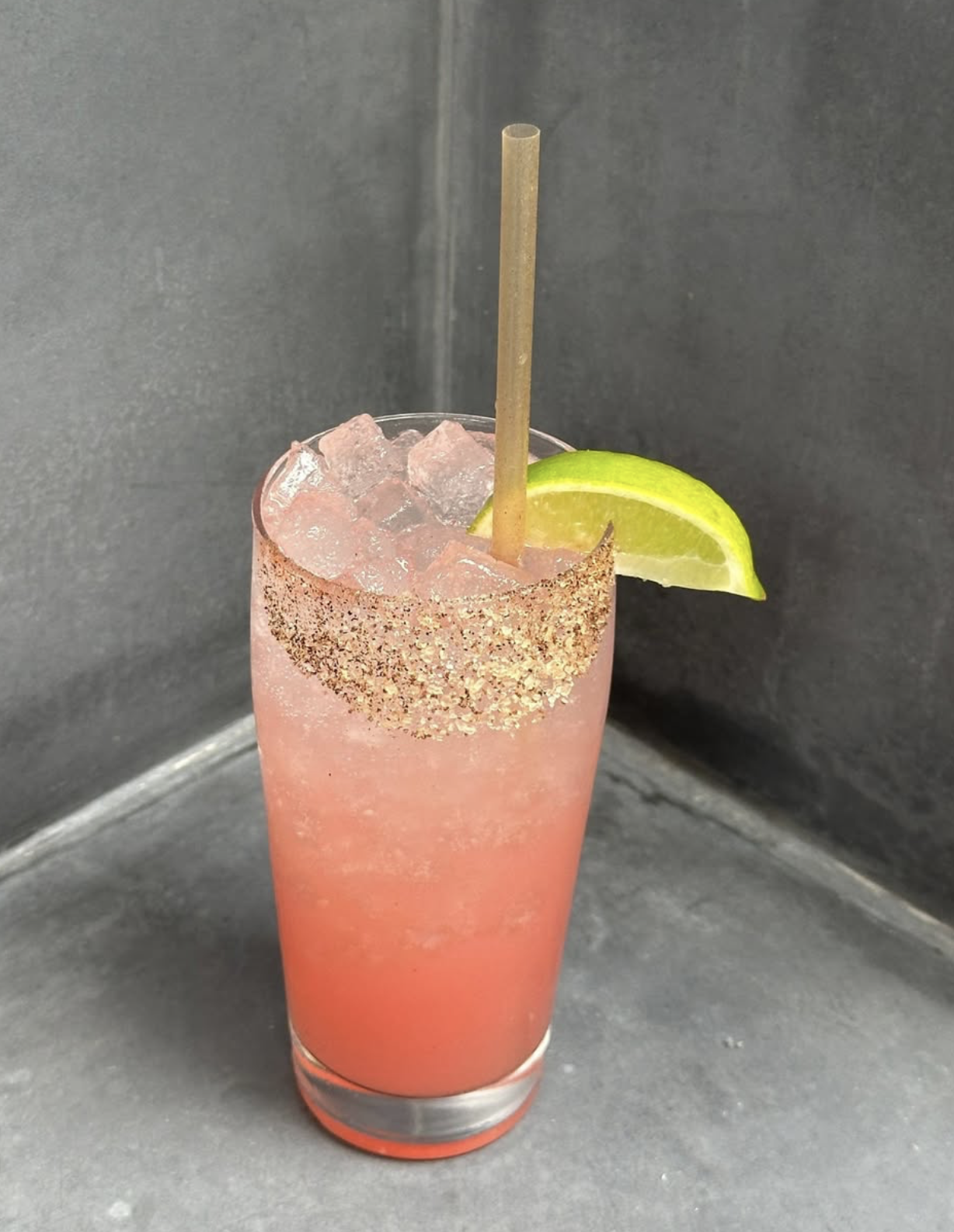 Iced pink cocktail with a lime wedge, straw, and spiced rim.