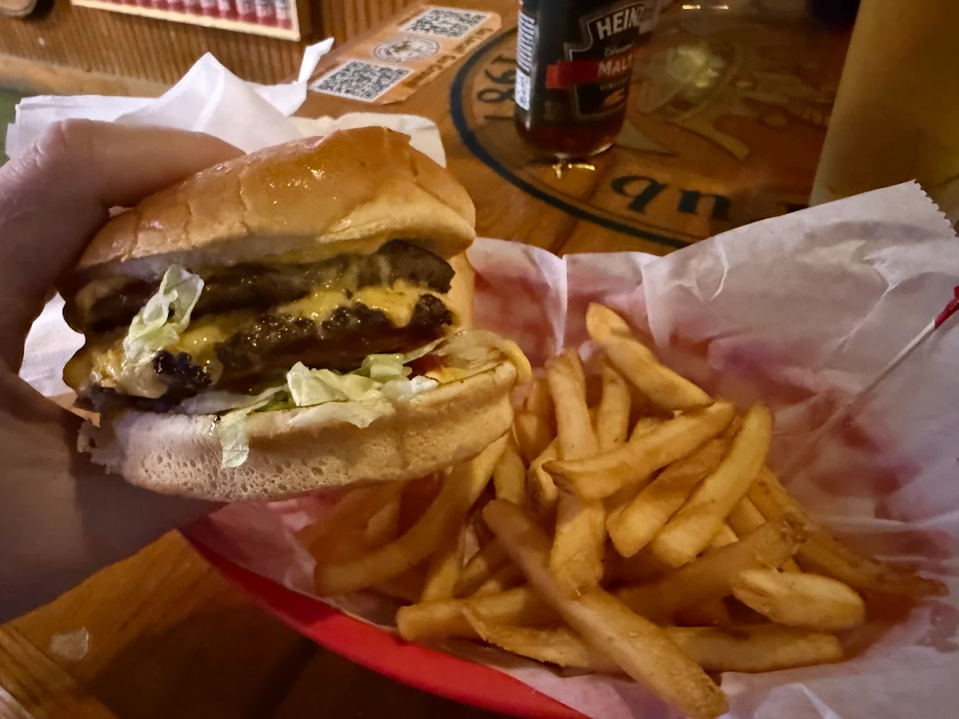 Hand holding a double cheeseburger with lettuce, served with fries.