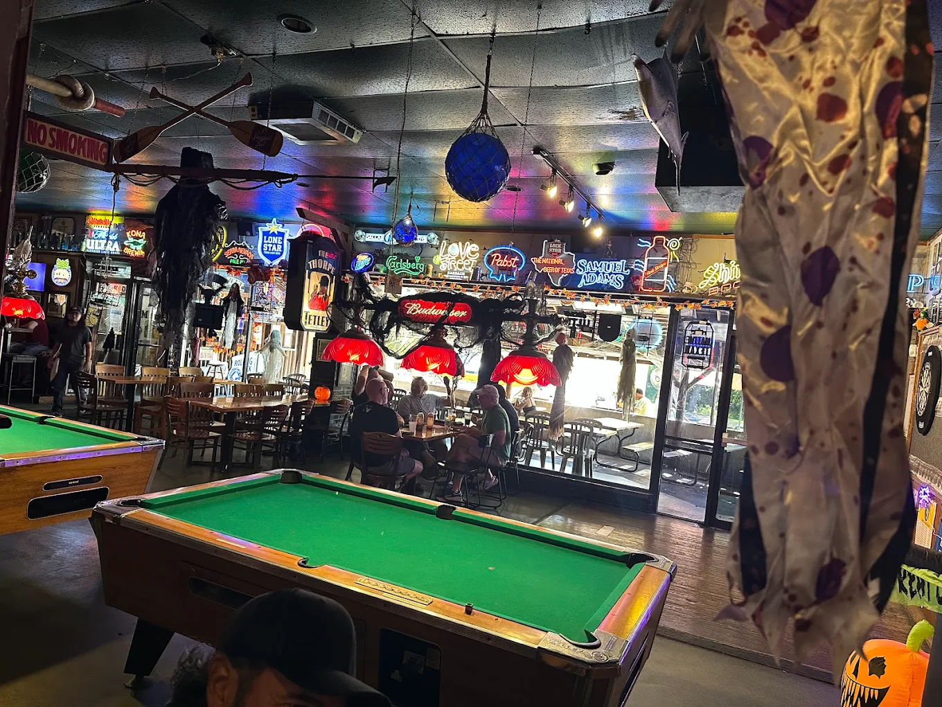 Bar interior with pool tables, neon signs, and Halloween decor.