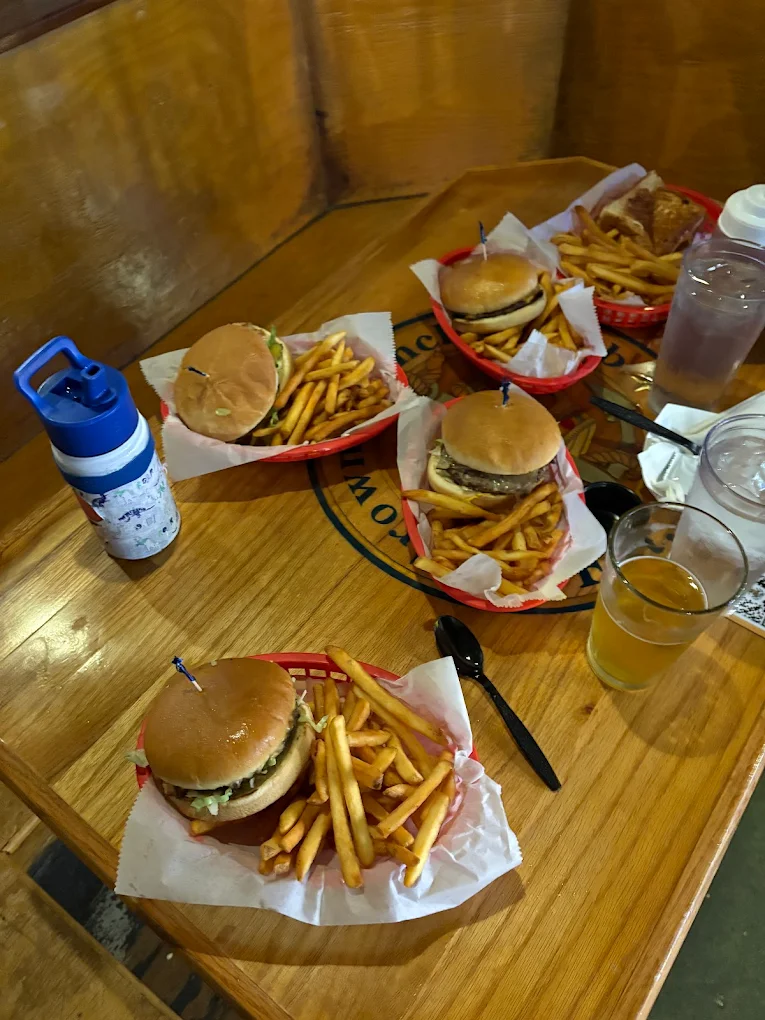 Multiple burgers and fries with drinks on a wooden table.