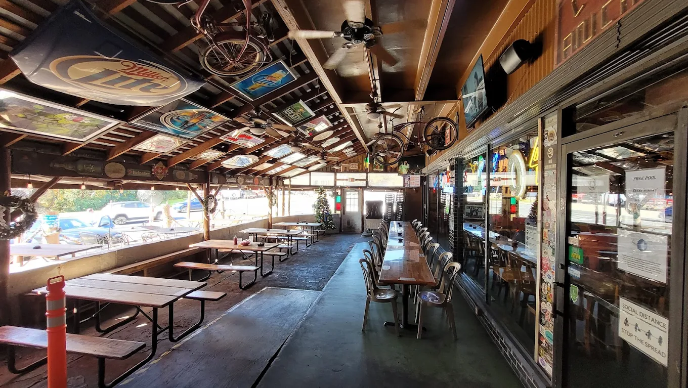 Rustic bar patio with picnic tables, a long bar, and ceiling decor.