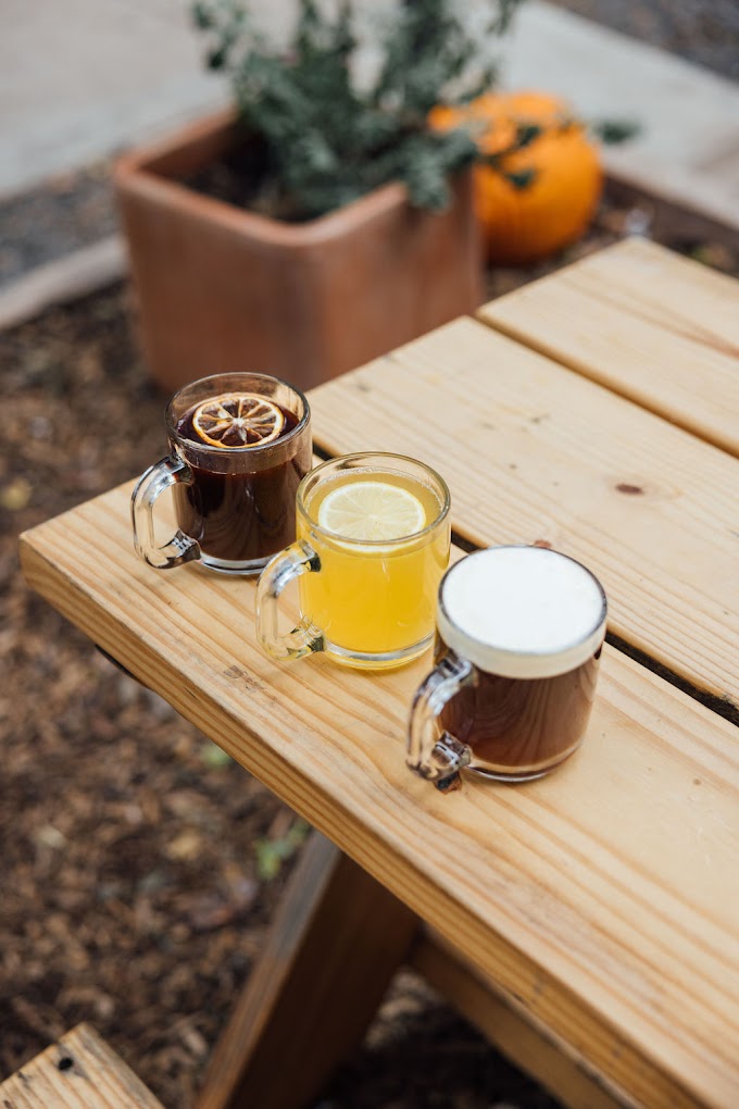 Three drinks in glass mugs on an outdoor wooden table.