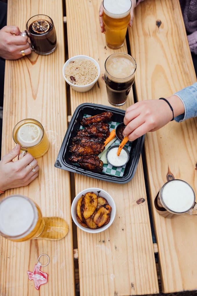 Hands around a wooden table with chicken wings, rice, and beer.