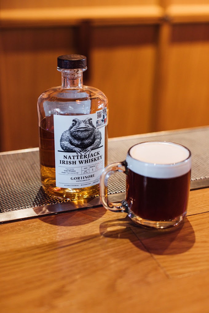 Natterjack Irish Whiskey bottle next to a dark drink with white foam.