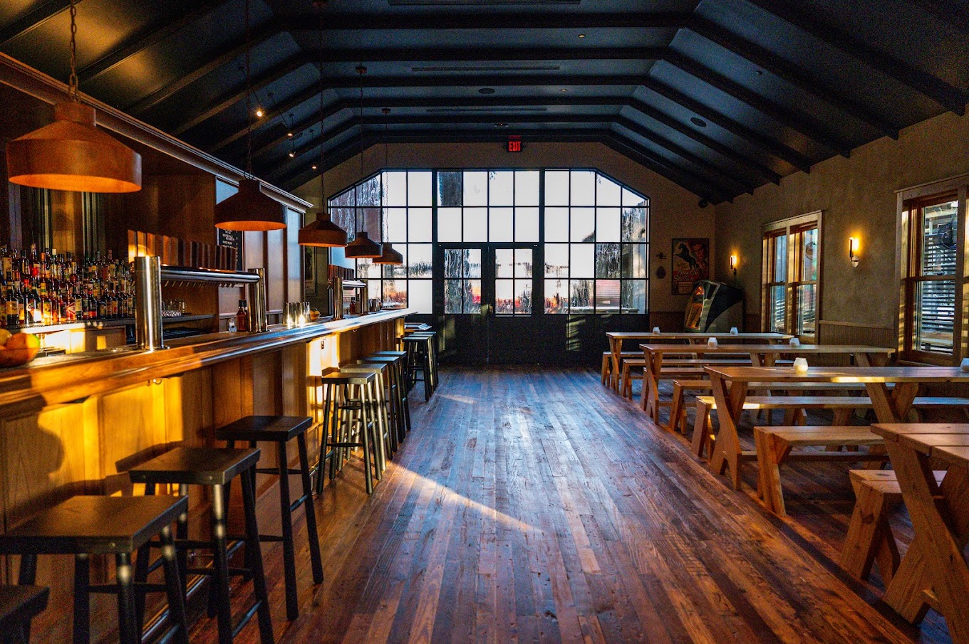 Empty restaurant interior with wooden bar, tables, and large window.