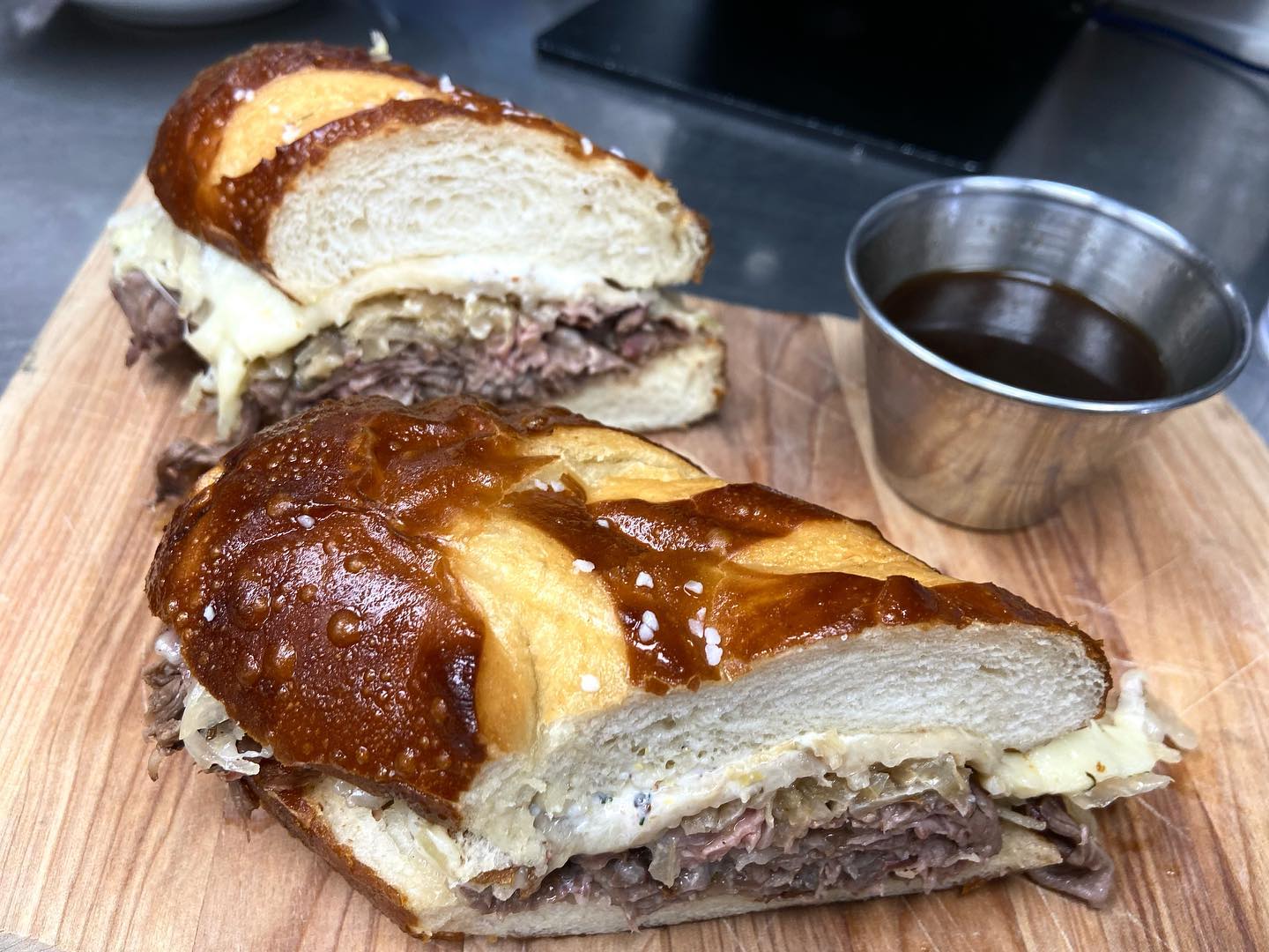 Two pretzel bun sandwiches with meat, melted cheese, and dipping sauce.