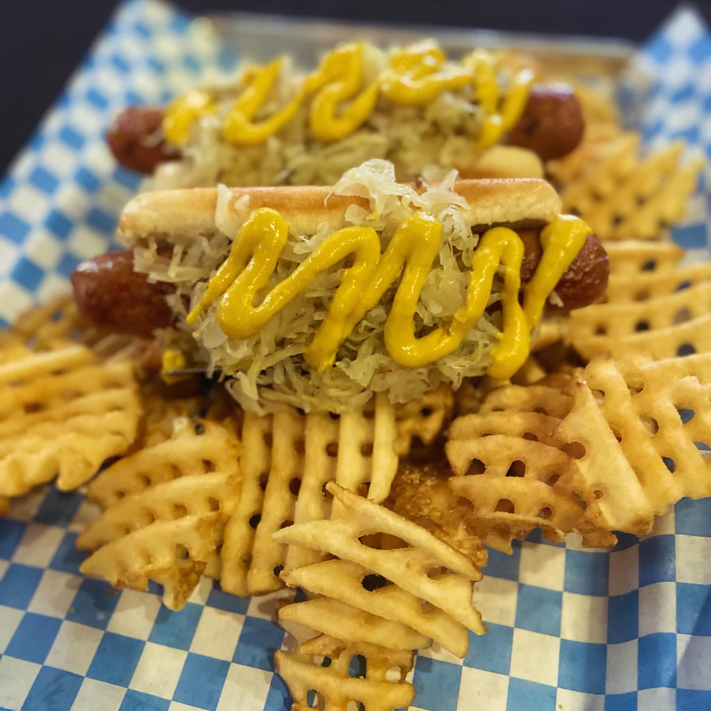 Two hot dogs with sauerkraut, mustard, and waffle fries.