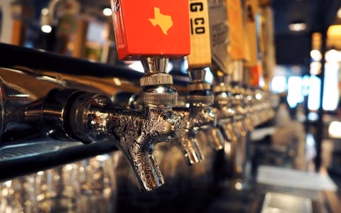 A row of chrome beer taps with condensation, one handle shows Texas.