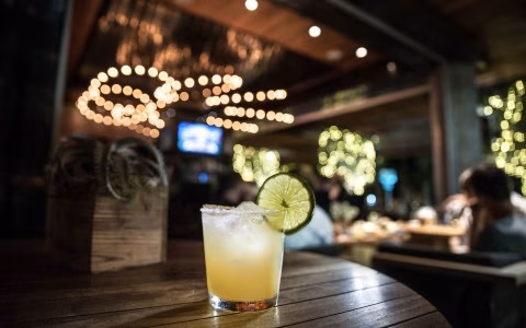 Cocktail with lime and salt rim on a wooden table at night.