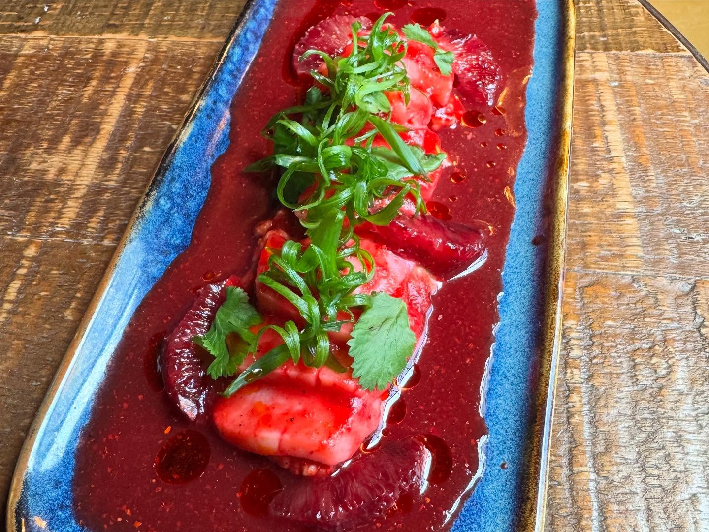 White food on blue plate in red sauce, blood orange, green herbs.