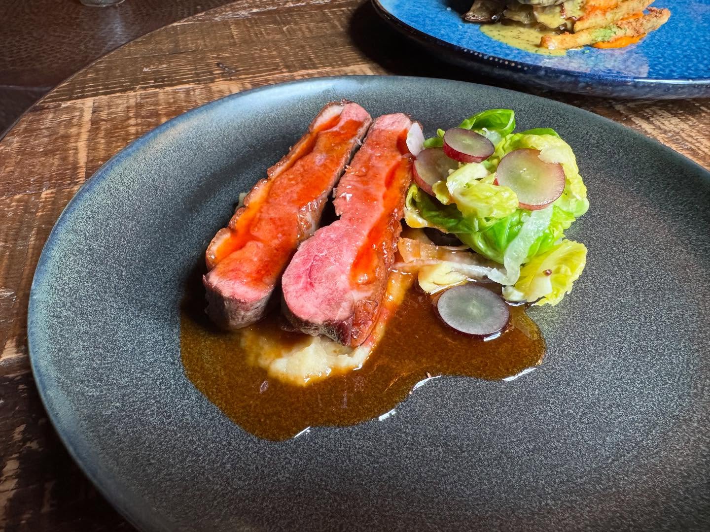 Sliced red meat, mashed potatoes, and lettuce with grapes on a plate.