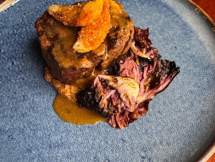 Cooked meat with sauce, crispy topping, and charred radicchio on blue plate.