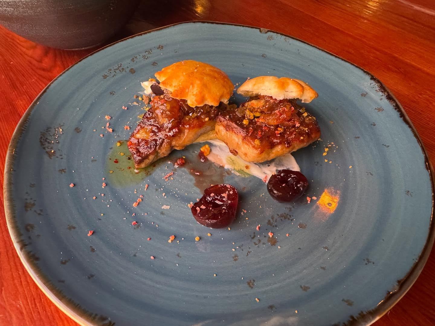 Two seared portions topped with relish, pastry, and cherries on a blue plate.