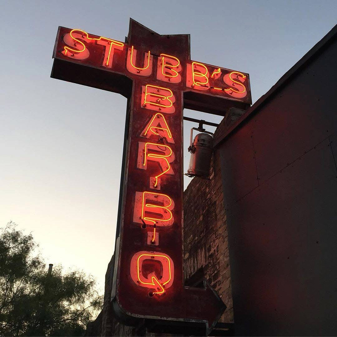 Vintage red neon sign for Stubb's Bar-B-Q against a pale sky.