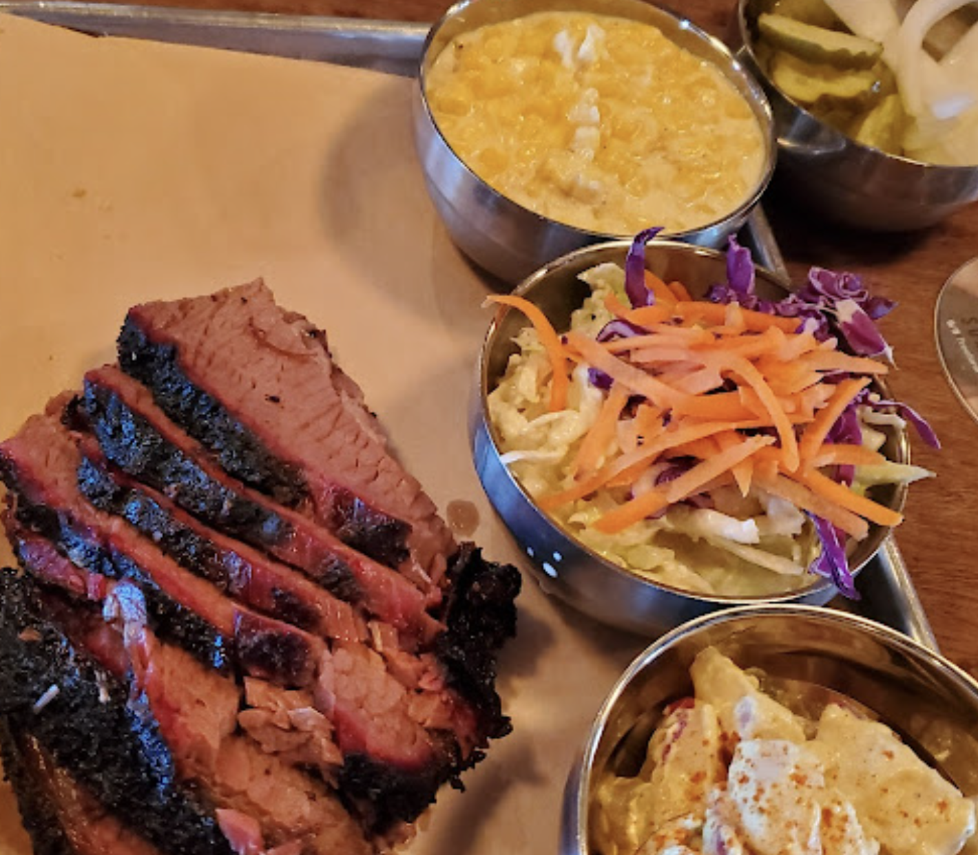 Sliced smoked brisket with corn, coleslaw, pickles, and potato salad.