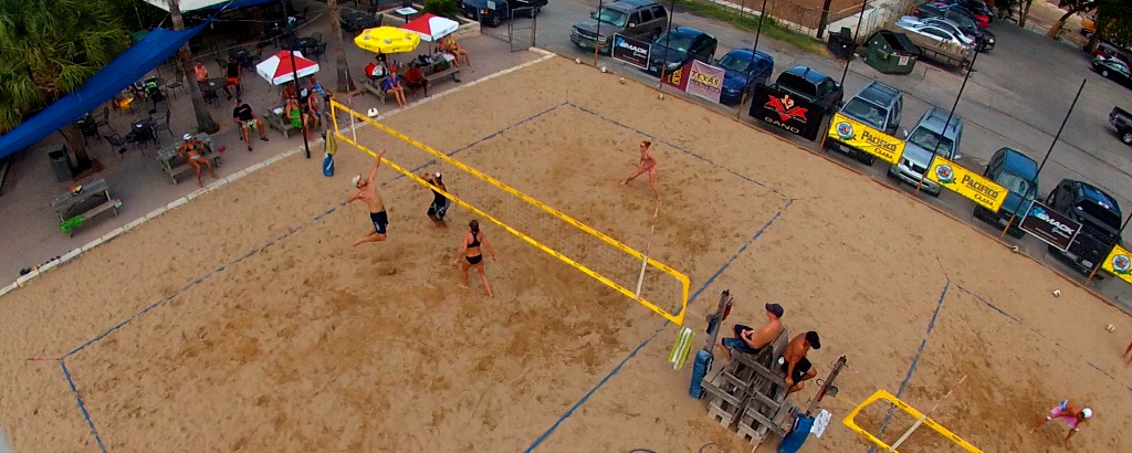 People playing beach volleyball on an outdoor sand court.