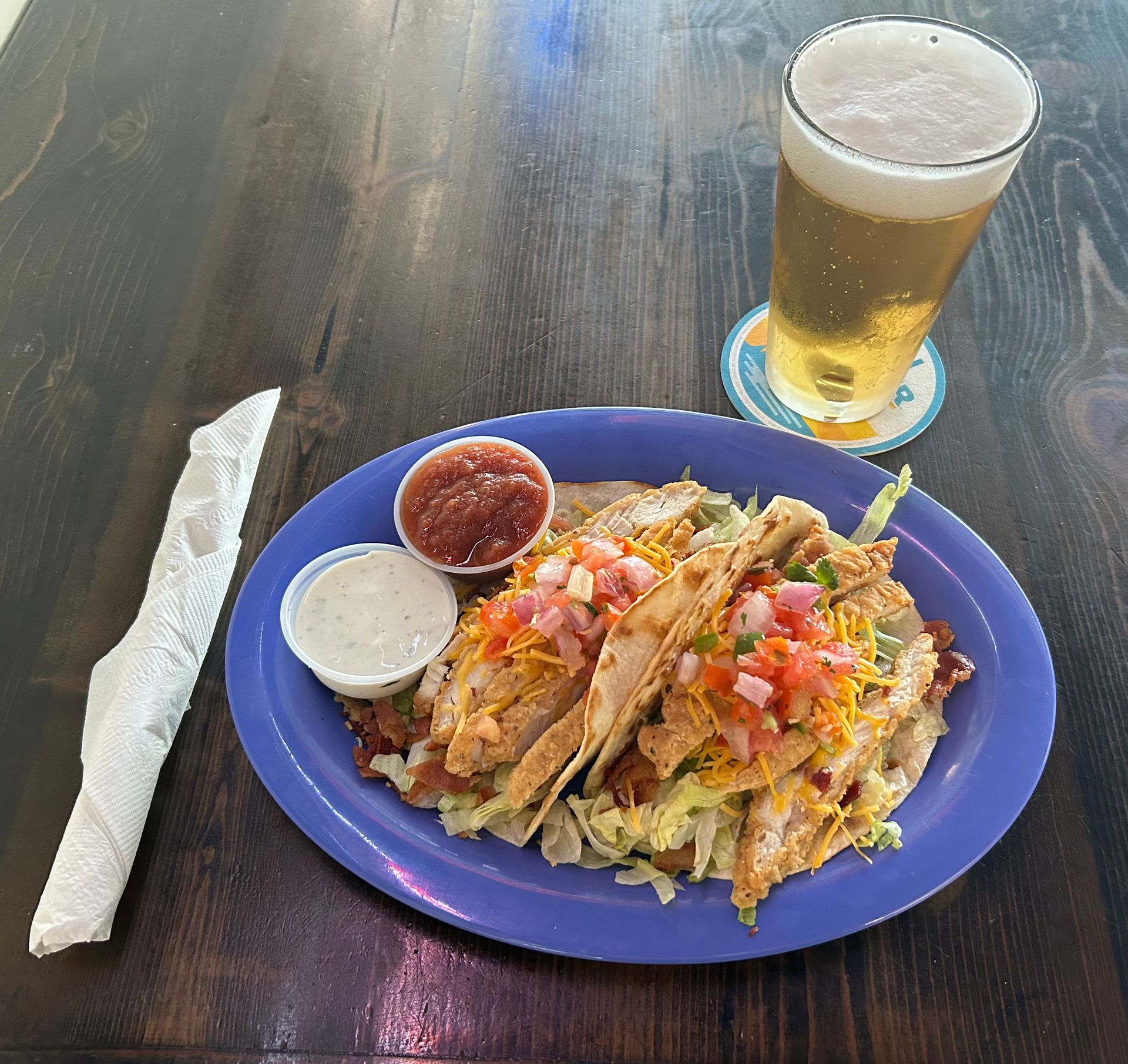 Two tacos, salsa, creamy sauce, and beer on a dark table.