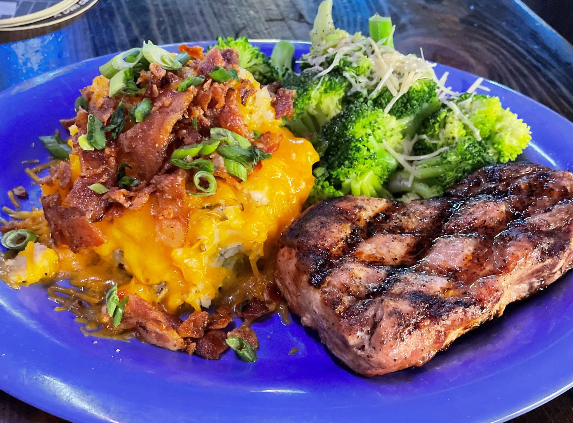 Grilled meat, cheesy bacon potato, and broccoli on blue plate.
