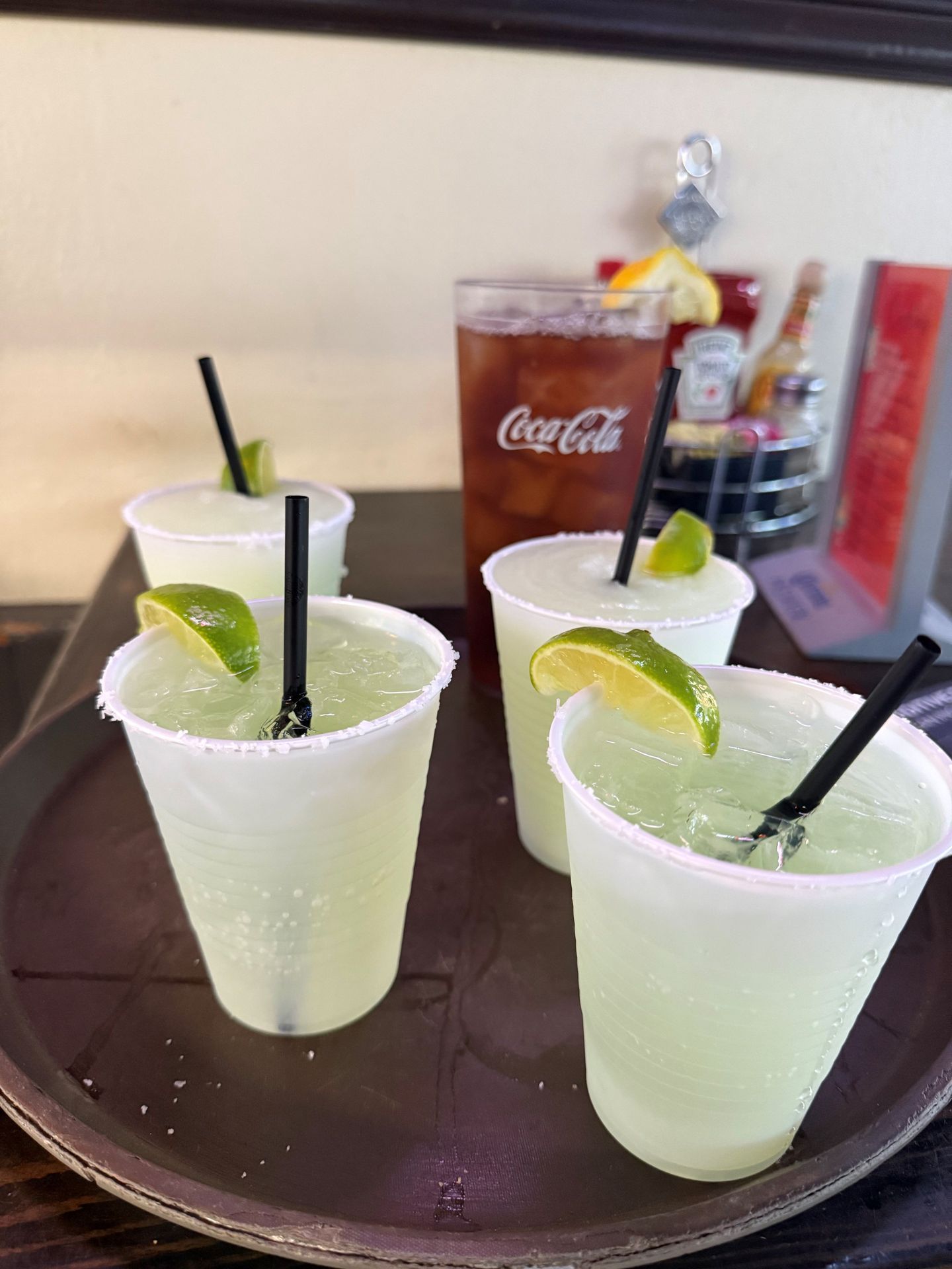 Four salt-rimmed margaritas with lime, and a Coca-Cola, on a tray.