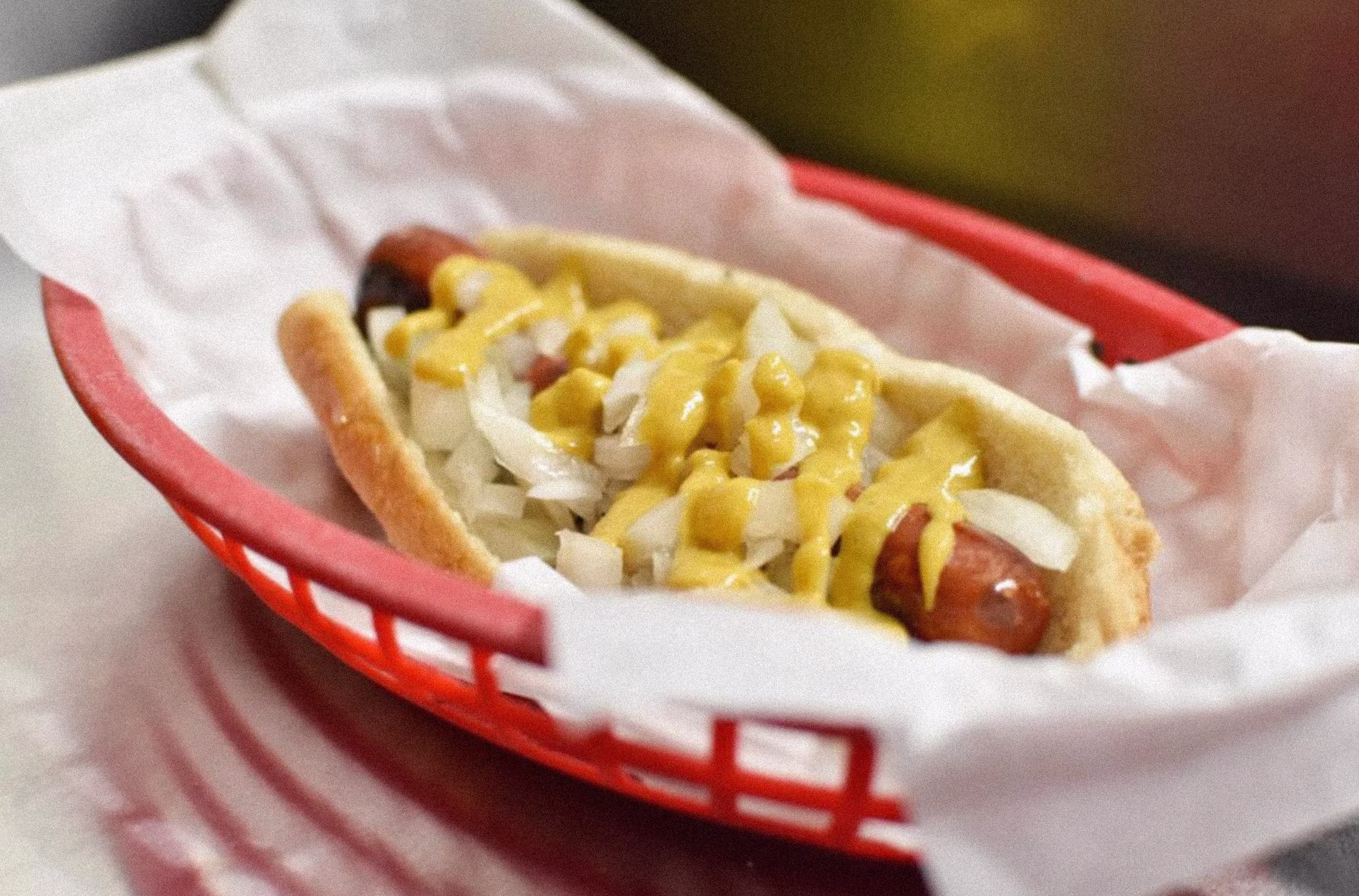 Hot dog with mustard and onions in a red plastic basket.