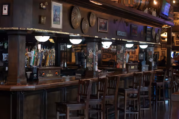 Empty traditional bar interior with wooden counter, stools, and beer taps.