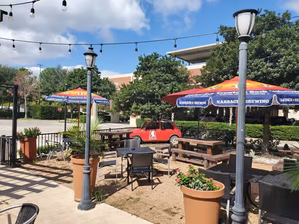 Outdoor patio with tables, Karbach Brewing umbrellas, string lights, and red car.