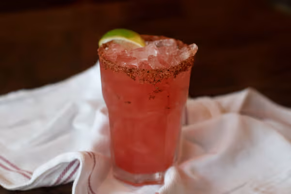 Red drink with crushed ice, a spiced rim, and lime garnish.