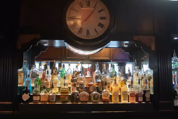A large clock above a bar with many bottles of liquor.