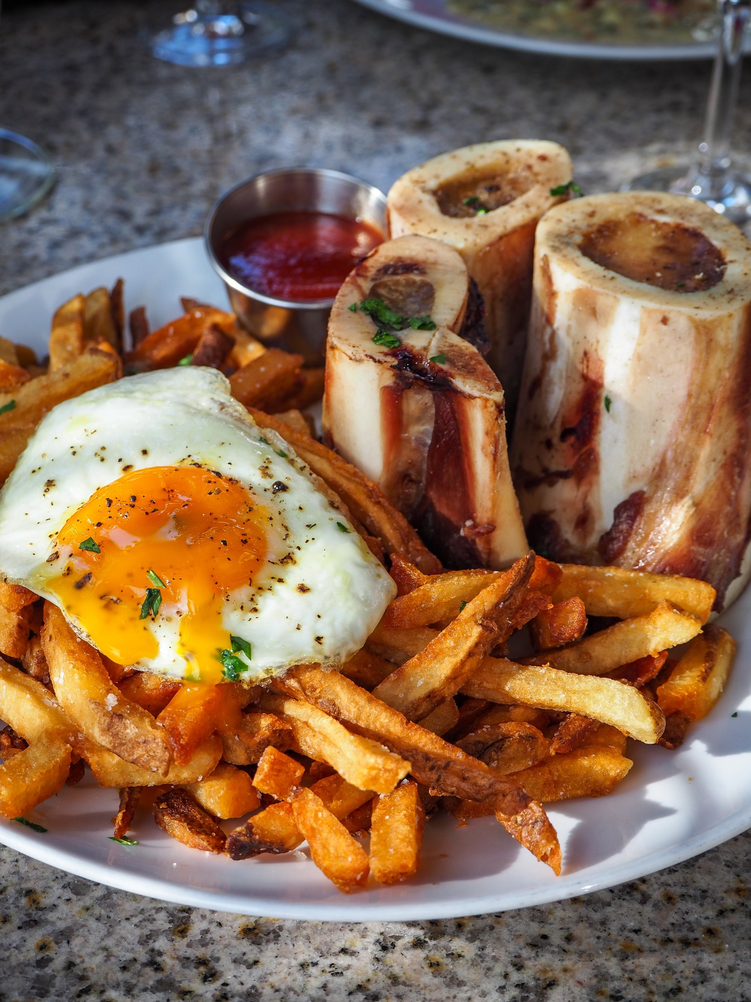 Bone marrow with a sunny-side up egg, fries, and ketchup.