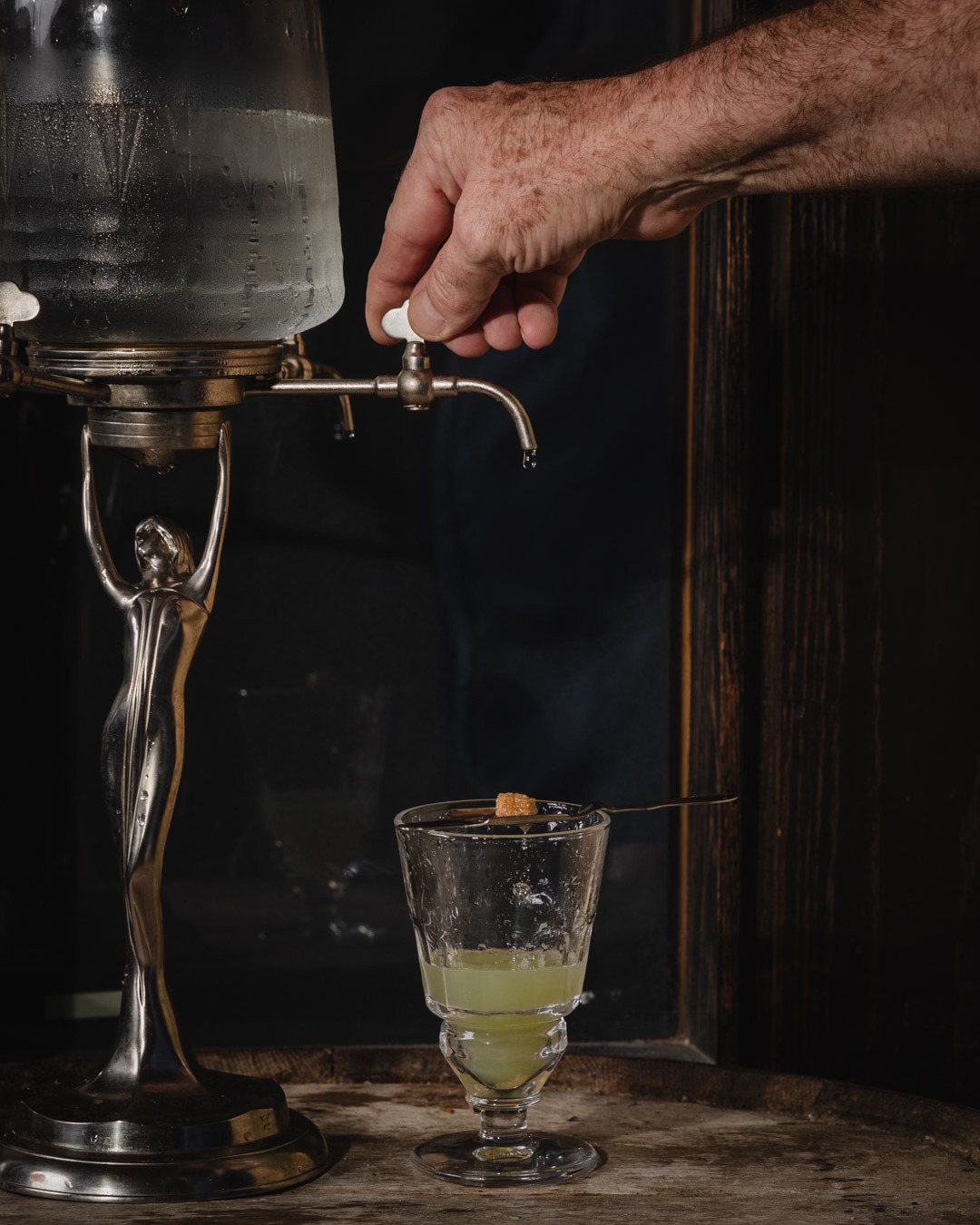 Hand turning absinthe fountain tap, water dripping onto sugar cube.