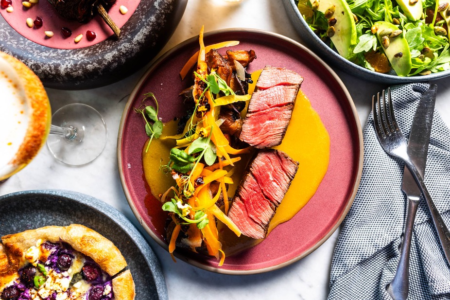 Table spread with rare steak, salad, and a blueberry tart.