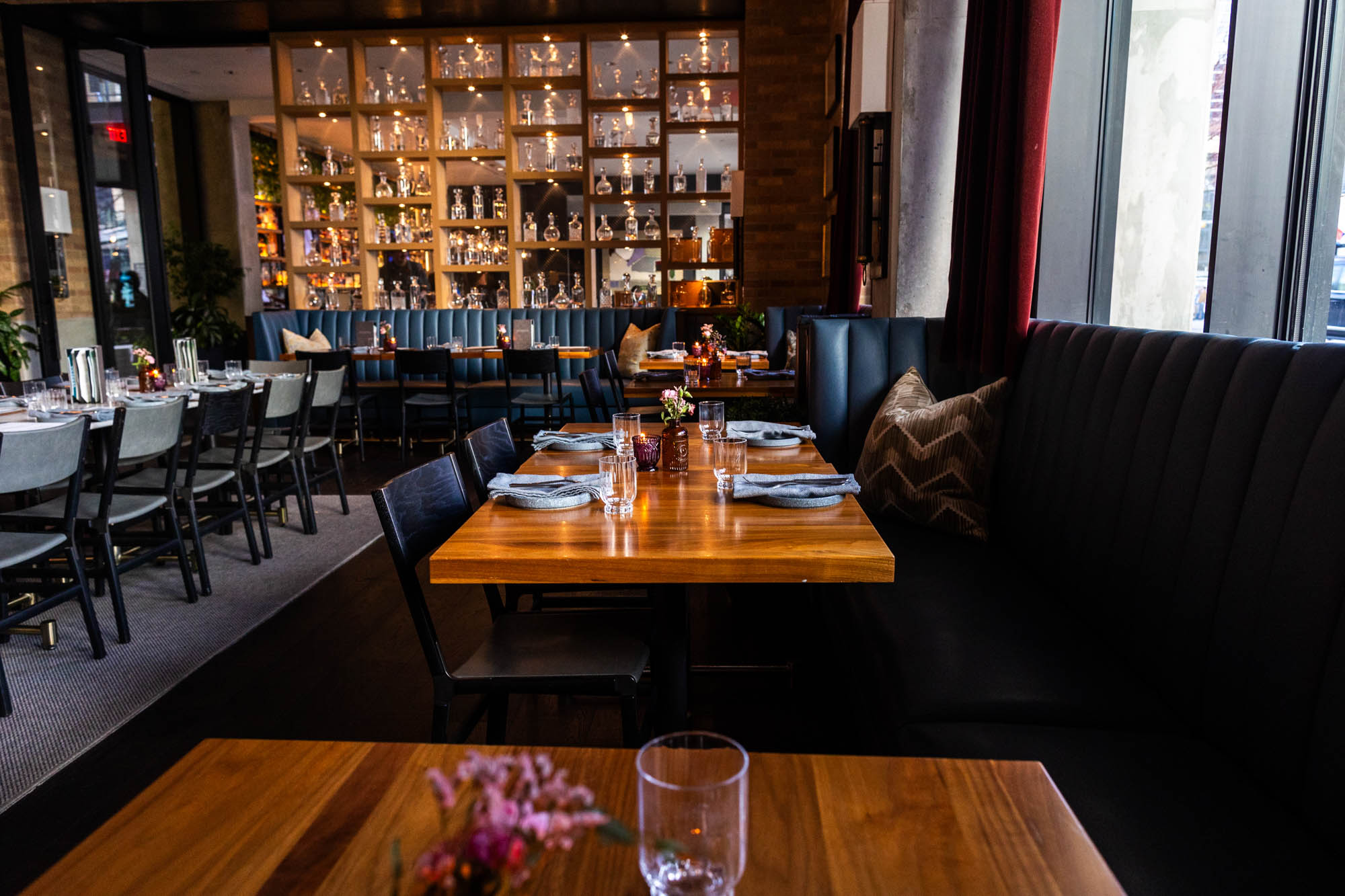 Tables and dark booths in a restaurant with a backlit bottle wall.