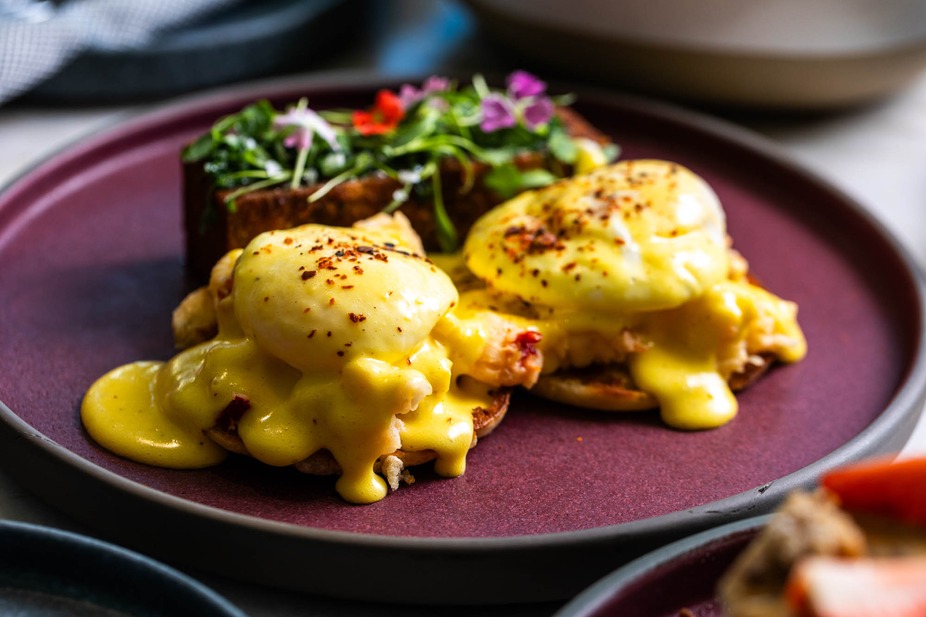 Two eggs Benedict with hollandaise, beside garnished bread.