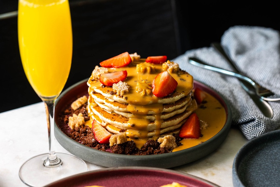 Pancakes with strawberries and yellow sauce, next to an orange drink.