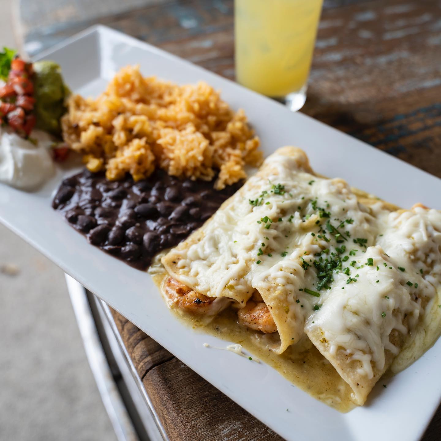 Enchiladas, rice, black beans, guacamole, salsa, sour cream on a white plate.