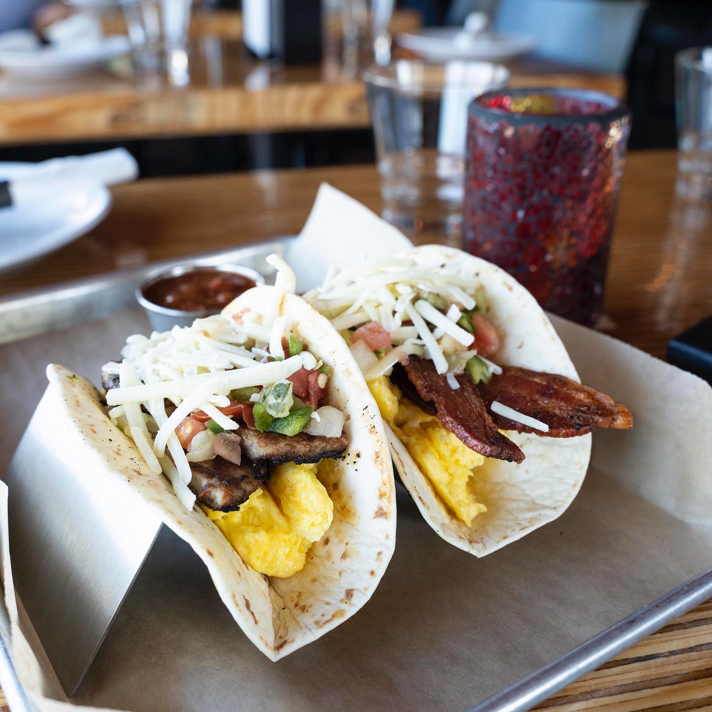Two breakfast tacos with eggs, meat, cheese, and salsa on a tray.