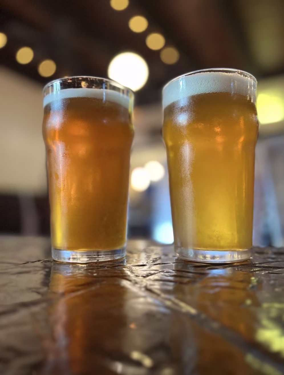 Two glasses of golden liquid with foam and condensation.