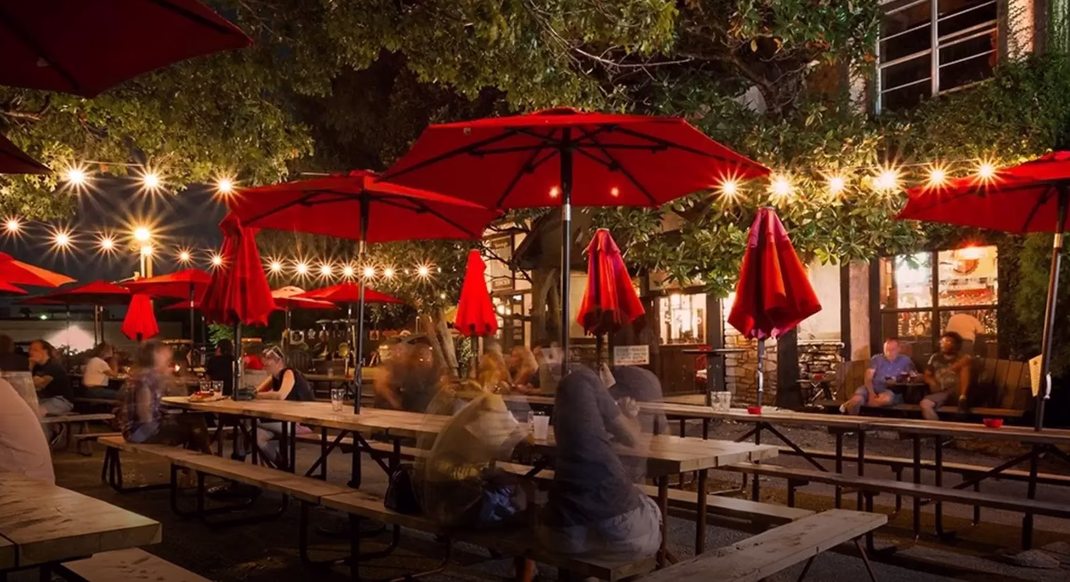 Outdoor restaurant patio at night with red umbrellas and string lights.