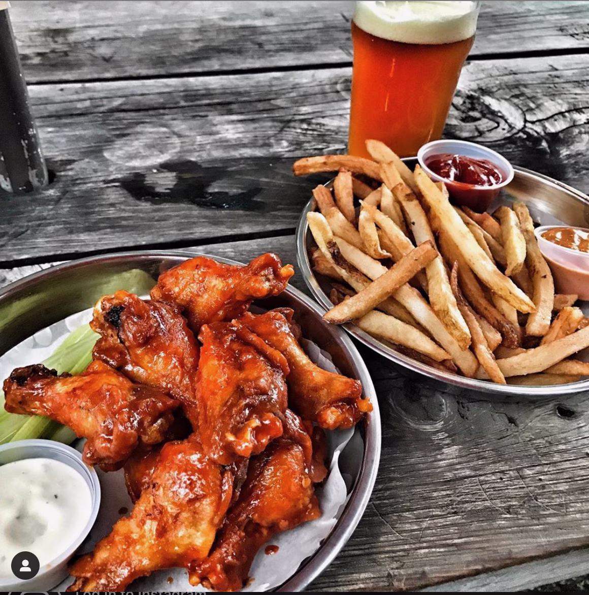 Buffalo wings, french fries, and a beer on a wooden table.