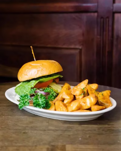 Hamburger, potato wedges, and parsley on a white oval plate.
