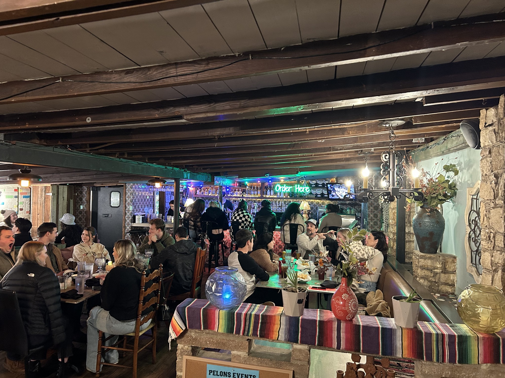 A bustling restaurant scene with diners, a bar, and exposed ceiling beams.