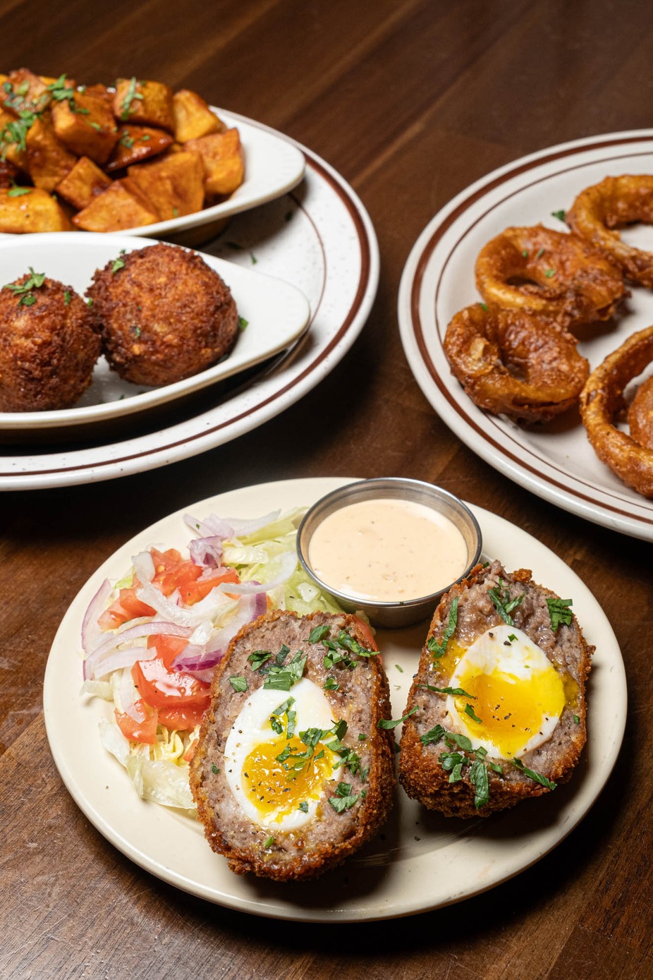 Halved Scotch eggs with runny yolks, side salad, and dipping sauce.