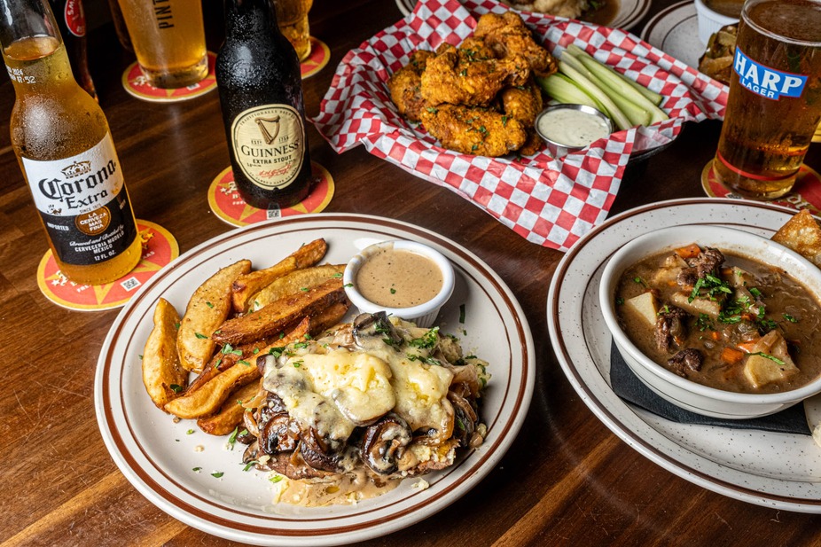 Pub table with steak, stew, chicken wings, and multiple beer bottles.