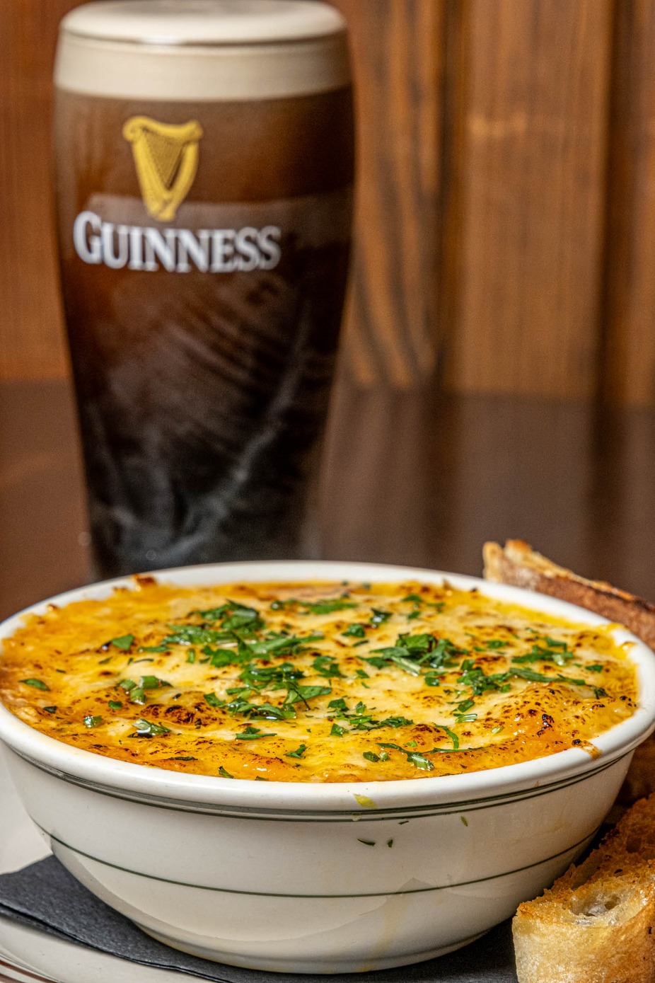 Baked cheesy dish with parsley, toast, and a Guinness beer.