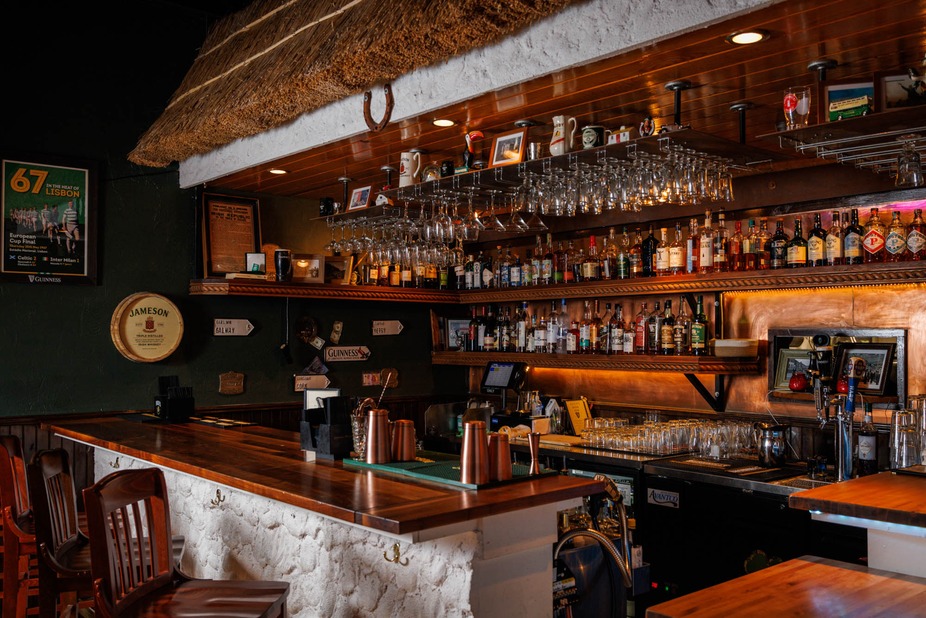 Irish pub interior with wooden bar, many liquor bottles, and thatched roof.