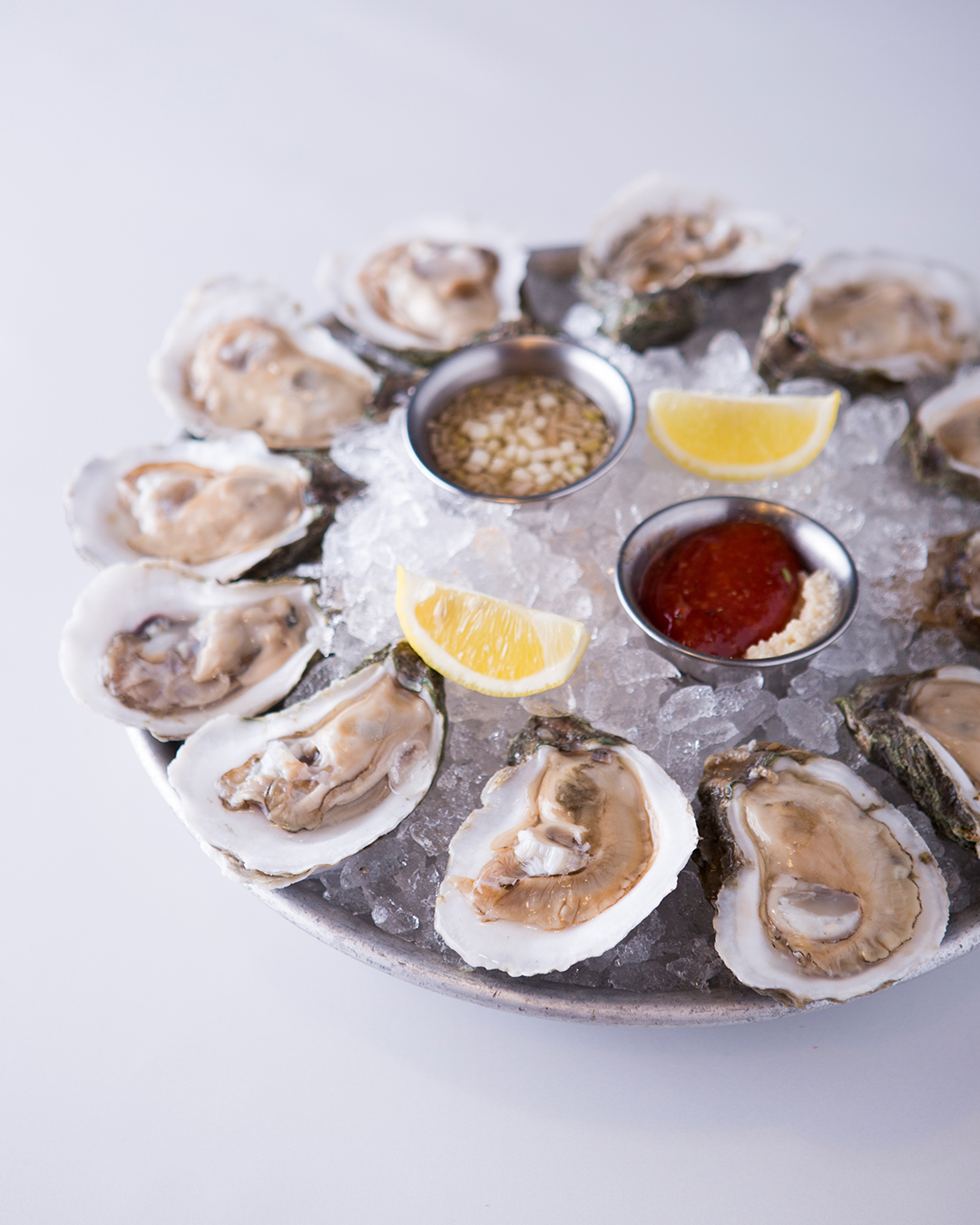 Raw oysters on ice with lemon wedges and two dipping sauces.
