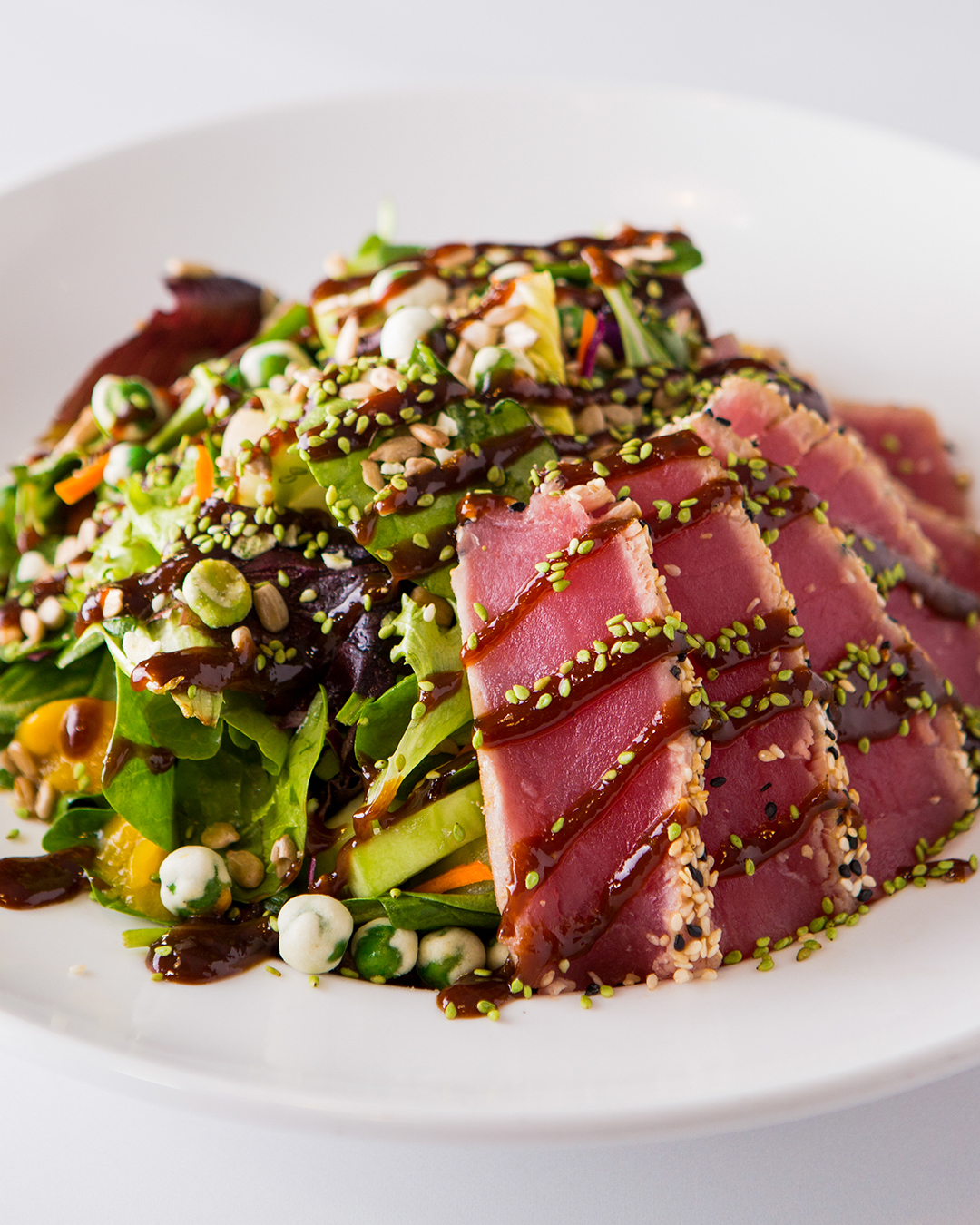 Seared tuna with sesame seeds and dressing on a green salad.