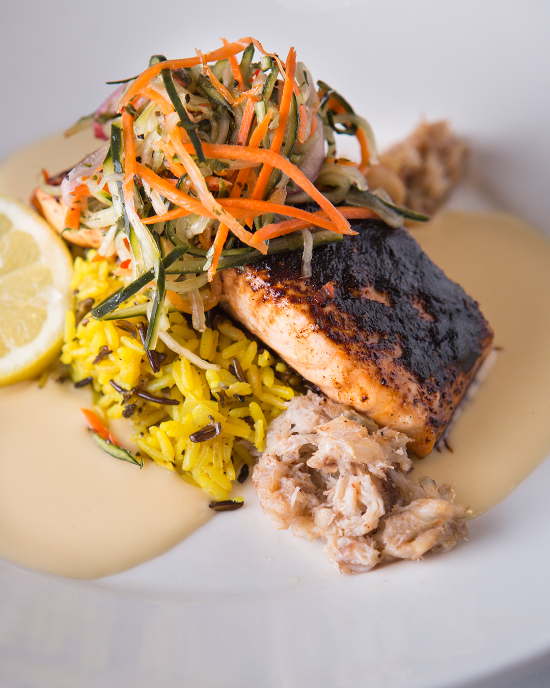 Seared salmon, julienned vegetables, yellow rice, crab meat, lemon, and sauce.