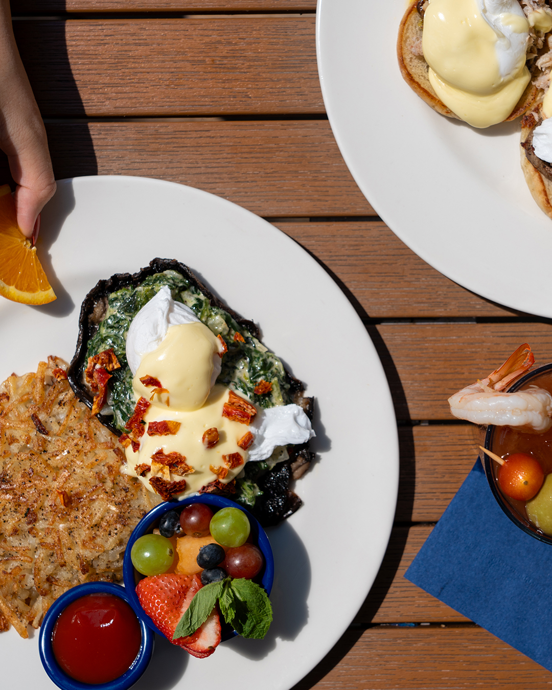 Overhead view of breakfast plates with eggs, hash browns, fruit, and a drink.