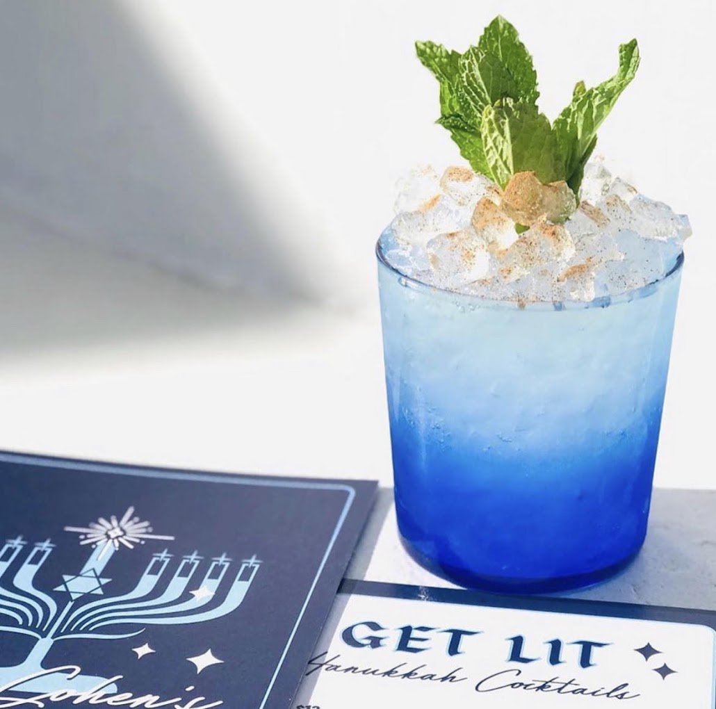 Blue ombré cocktail with ice and mint, beside Hanukkah menu.